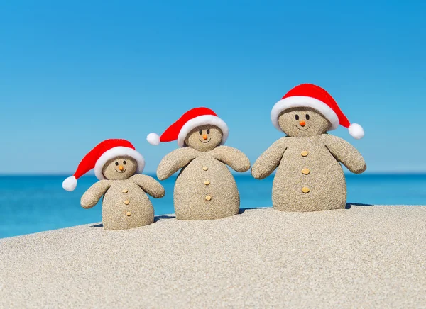 Natale sabbia pupazzi di neve famiglia a Santa cappelli sulla spiaggia dell'oceano — Foto Stock