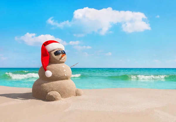 Christmas Snowman in Santa hat and sunglasses at sea beach — Stock Photo, Image