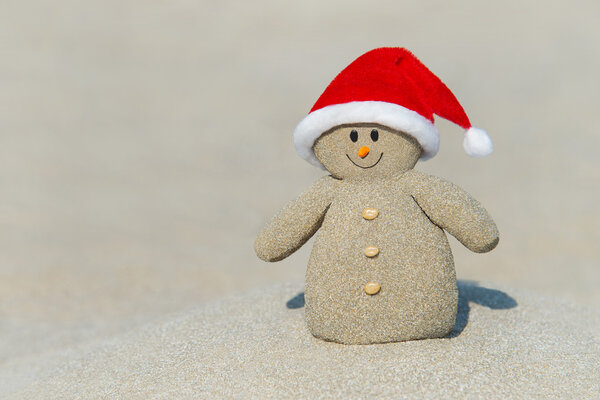 Snowman in Christmas Santa Claus hat at ocean beach sand