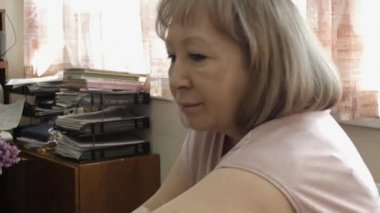 Yaşlı bir kadın bir odada oturuyor, başka tarafa bakıyor ve birileriyle konuşuyor. Yakın plan..