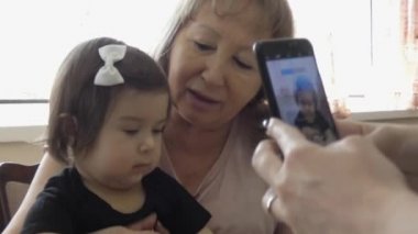 Büyükanne ve küçük torun birlikte oturup bir şeyler izliyorlar. Şu anda, başka bir kadının elleri çocuğun telefonunda fotoğraflanıyor..