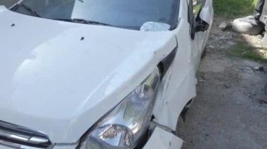 Çarpışan beyaz bir araba, sol tarafı ezilmiş ve yan aynası kırılmış..