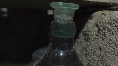 Cam tıpası ile tıpalanmış büyük cam bir şarap şişesinin boynu. Bir toprak şarap mahzeninde, eski bir şişe ev yapımı şarap, çok eski. Yakın plan.