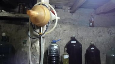 Eski bir evde, topraksı bir şarap mahzeni. Tıpalanmış şarap şişeleri ve farklı boyutlarda boş cam şişeler var..