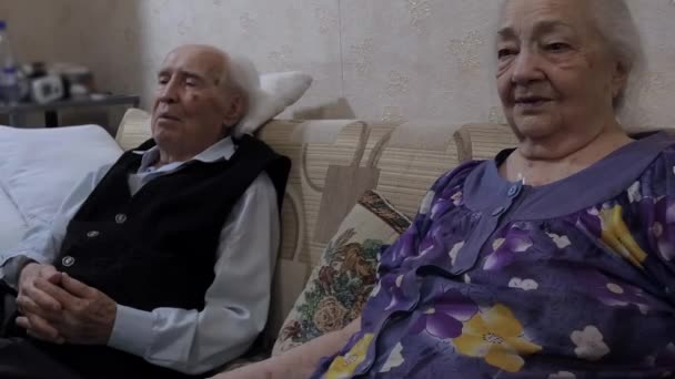 老人夫婦 男性と女性は 自宅のソファの上に座っています 彼らは興味を持って一緒に何かを見ている — ストック動画