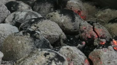 Küflenmiş kömür parçaları yanıyor. Kömürler hafif bir kül tabakasıyla kaplıdır. Havanın hareketi kıvılcımlar ve kül parçacıkları saçar. Yakın plan..