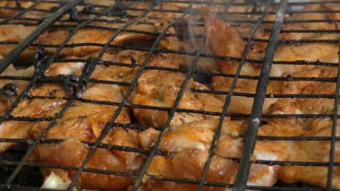 Izgarada tavuk ızgarasının yakın çekimi. Tavuk kanatları ızgarada pişirilir. Izgara ızgarası diğer tarafa çevrilmiş. Etin üzerinde mis kokulu bir duman yükseliyor..