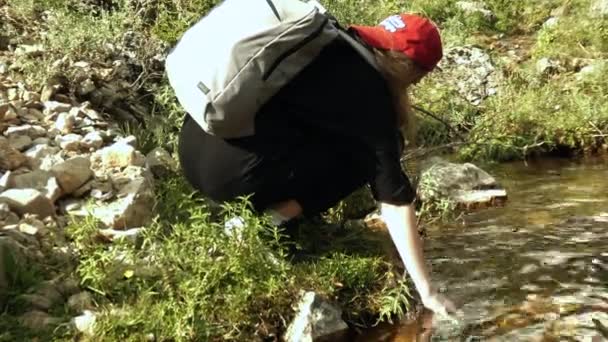 A female hiker is drawing water from a mountain river. — Stock Video