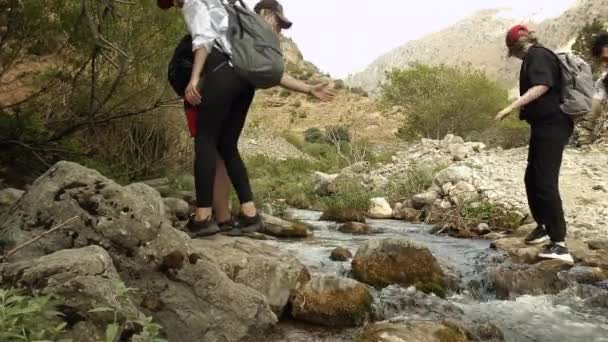 若い観光客のグループは、岩の上に山の川を渡っている. — ストック動画