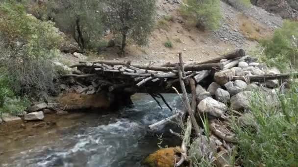 Egy öreg, görbe fahíd egy viharos hegyi folyó felett. — Stock videók