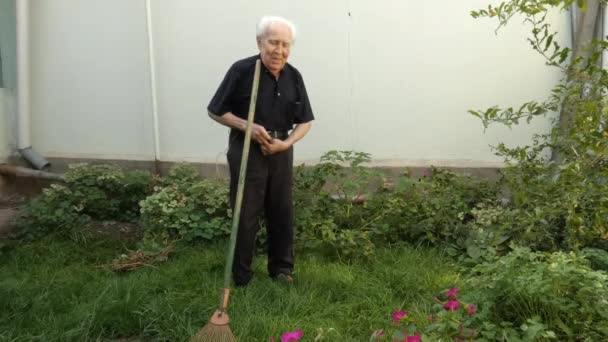 En gammal man justerar bältet på byxorna medan han arbetar i sin trädgård. — Stockvideo