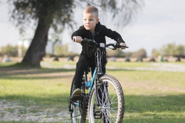 Siyahlı sarı saçlı çocuk dışarıda bisikletinin üstünde oturuyor..