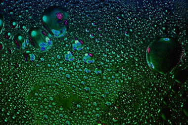 Renkli bulanık arkaplanda cam bir kapağın üzerindeki makine yağı damlacıklarının soyutlanması