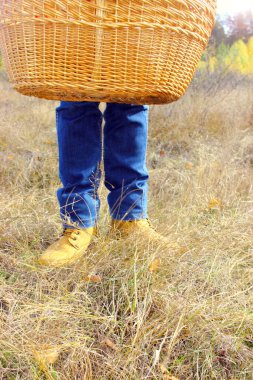 Sepet, kot pantolon ve bacaklarda kahverengi deri ayakkabılar, sonbahar çimlerinin arka planında, mevsimi değiştirme konsepti