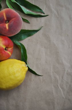Yaz meyvesi arka planı. Şeftali ve limonlu düz kompozisyon. El işi kağıdında yeşil yapraklı olgun sulu meyveler. Düz görünüm kopyalama alanı yatıyordu. Taze organik meyve vejetaryen yemeği. Hasat konsepti