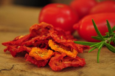 Kurutulmuş domates. Tahta bir arka planda duran güneşte kurutulmuş domatesler. Düz bir manzara. Dondurulmuş sebzeler. Kurutulmuş baharatlar sağlıklı yiyecekler. Baharatlar. Kurutulmuş İtalyan domatesi. Biberiye.