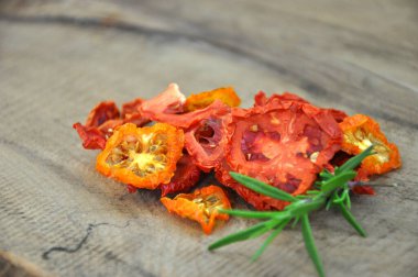 Kurutulmuş domates. Tahta bir arka planda duran güneşte kurutulmuş domatesler. Düz bir manzara. Dondurulmuş sebzeler. Kurutulmuş baharatlar sağlıklı yiyecekler. Baharatlar. Kurutulmuş İtalyan domatesi. Biberiye.