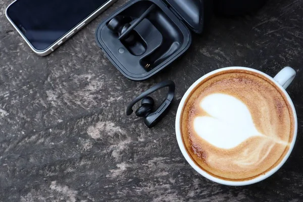 Coffee latte art milk foam on cup with smart phone and wireless bluetooth earphones