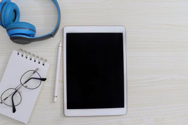 Tablet kalem, kulaklık ve gözlüklerle çalışma masasında.