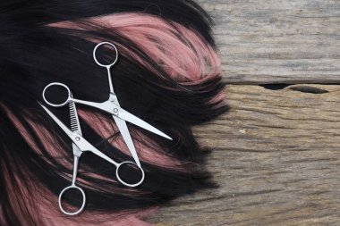 Hair cutting shears and black pink hair on brown wood table