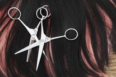 Hair cutting shears and black pink hair on brown wood table