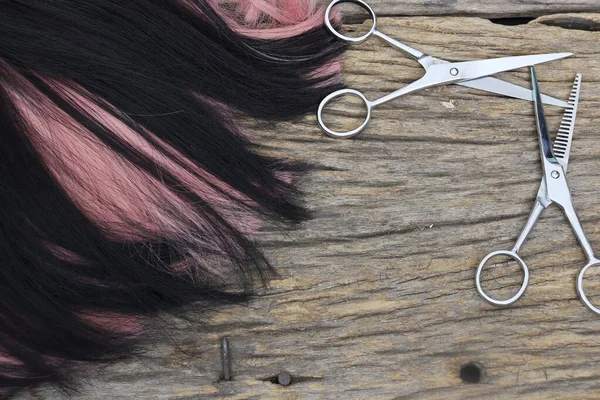 Hair cutting shears and black pink hair on brown wood table