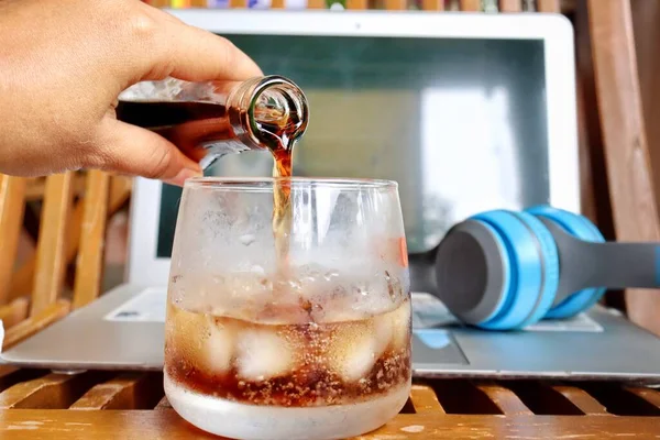 Pouring cola drink on glass and notebook with headphone work from home concept
