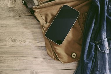 Ahşap arka planda kahverengi çantalı akıllı telefon ve ceket pantolonu.