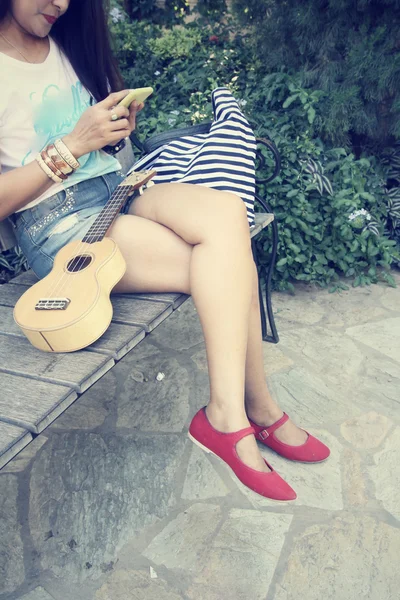 Mujer usando el teléfono inteligente con ukelele — Foto de Stock