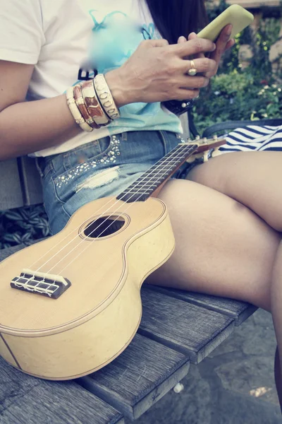 Женщина с помощью смартфона с укулеле — стоковое фото