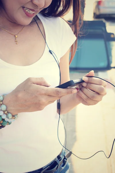 Mulher ouvindo música no fone de ouvido com telefone inteligente — Fotografia de Stock