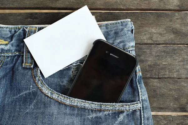 Teléfono inteligente con tarjeta en blanco en jeans — Foto de Stock