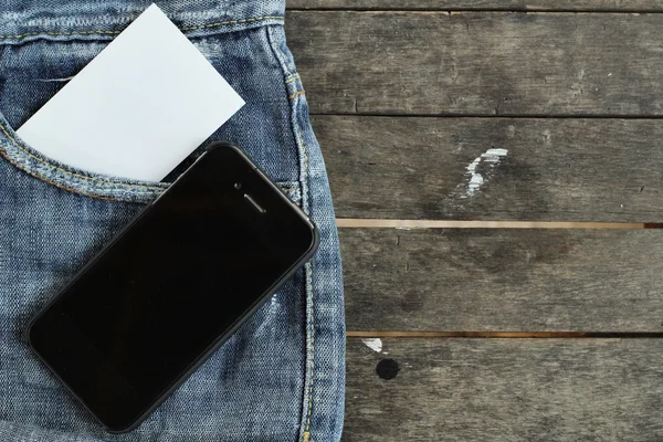 Telefone inteligente com cartão em branco em jeans — Fotografia de Stock