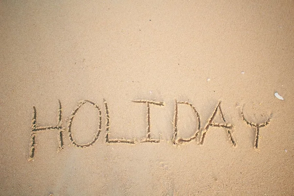 A palavra feriado escrito na areia na praia — Fotografia de Stock