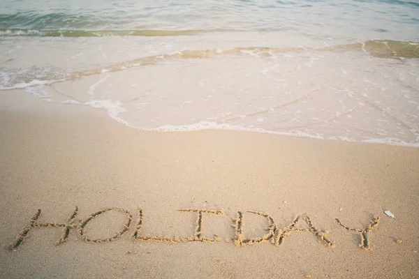 The word holiday written in sand on beach — Stock Photo, Image