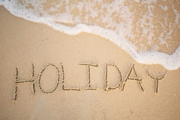 A palavra feriado escrito na areia na praia — Fotografia de Stock