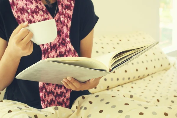 Woman drinking coffee with book sitting in bed — Stock Photo, Image