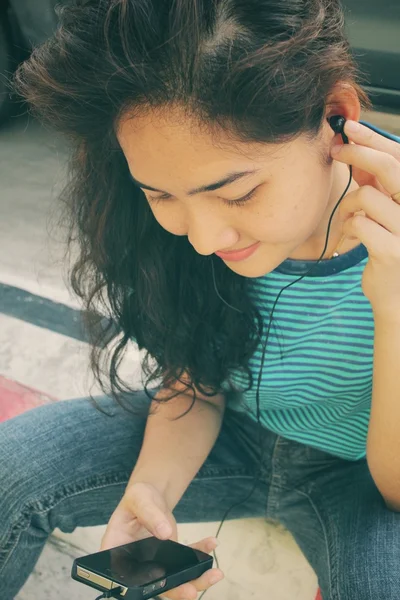 Ung kvinna lyssna på musik på hörluren med smart telefon — Stockfoto