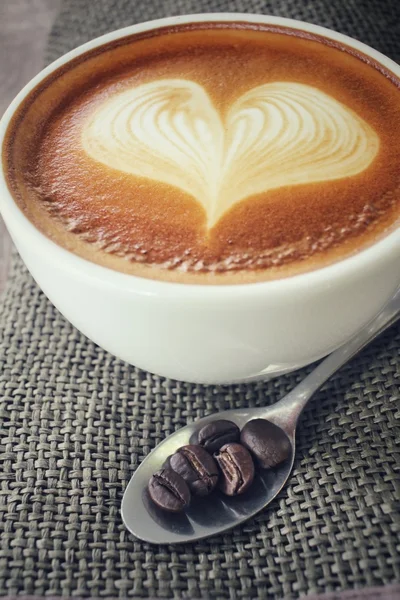 Vintage latte art coffee with beans — Stock Photo, Image