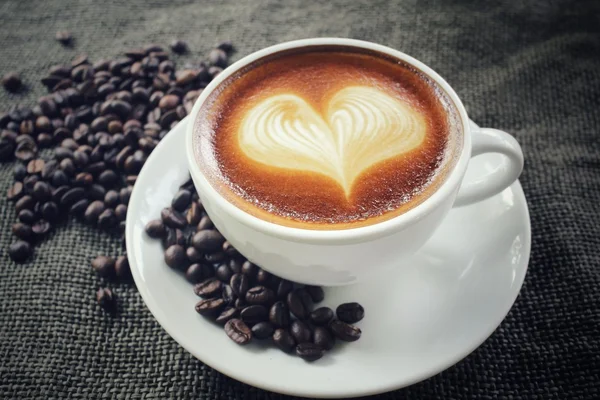 Vintage latte art coffee with beans — Stock Photo, Image