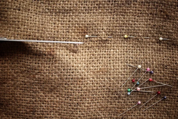 Colorful sewing pins with scissors on sackcloth
