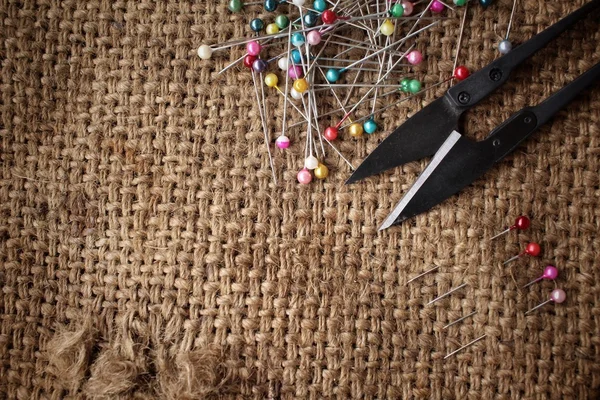 Pinos de costura coloridos com tesoura em pano de saco — Fotografia de Stock