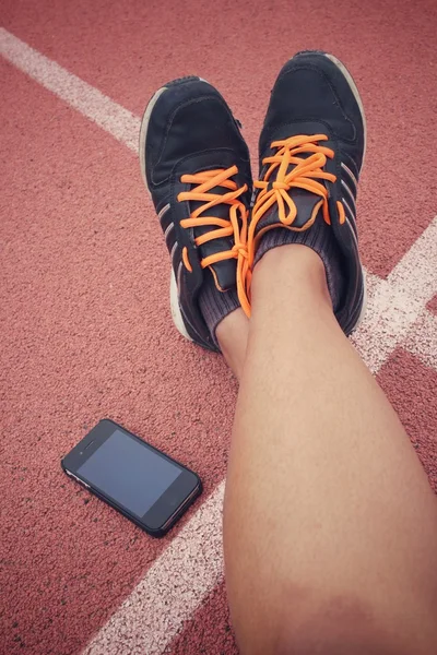 Zapatos deportivos con teléfono inteligente en pista — Foto de Stock