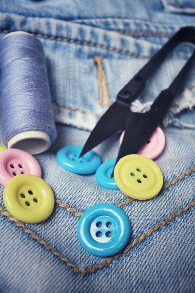 Colorful sewing buttons scissors and thread on jeans — Stock Photo, Image