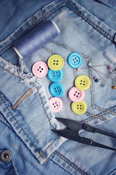 Colorful sewing buttons scissors and thread on jeans — Stock Photo, Image