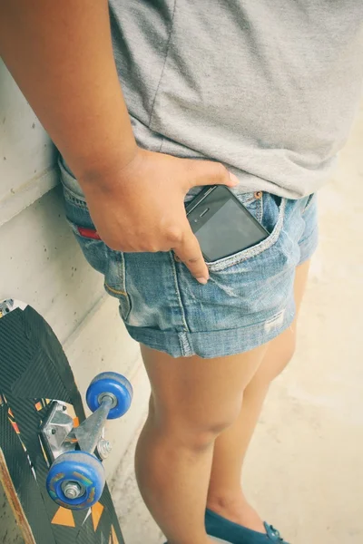 Slimme telefoon in jeans zak met skateboard — Stockfoto