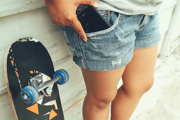 Smartphone in tasca jeans con skateboard — Foto Stock