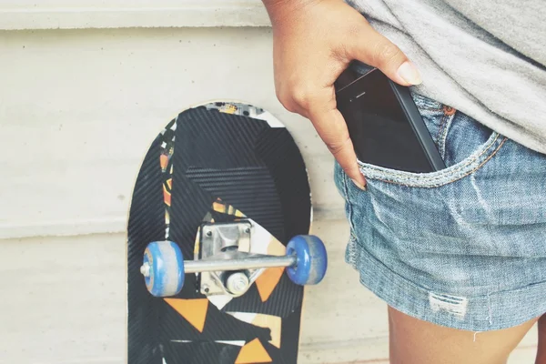 Smartphone in tasca jeans con skateboard — Foto Stock