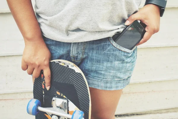 Smartphone in tasca jeans con skateboard — Foto Stock