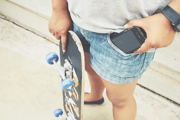 Smartphone in tasca jeans con skateboard — Foto Stock